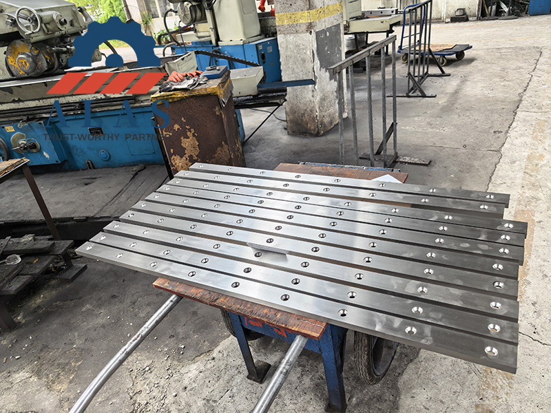 ALAS Manufacturing Plant: High-Volume Shear Blade Production ALAS制造车间堆放着一批经过精磨、带有沉孔安装孔的闸式剪板机刀片
